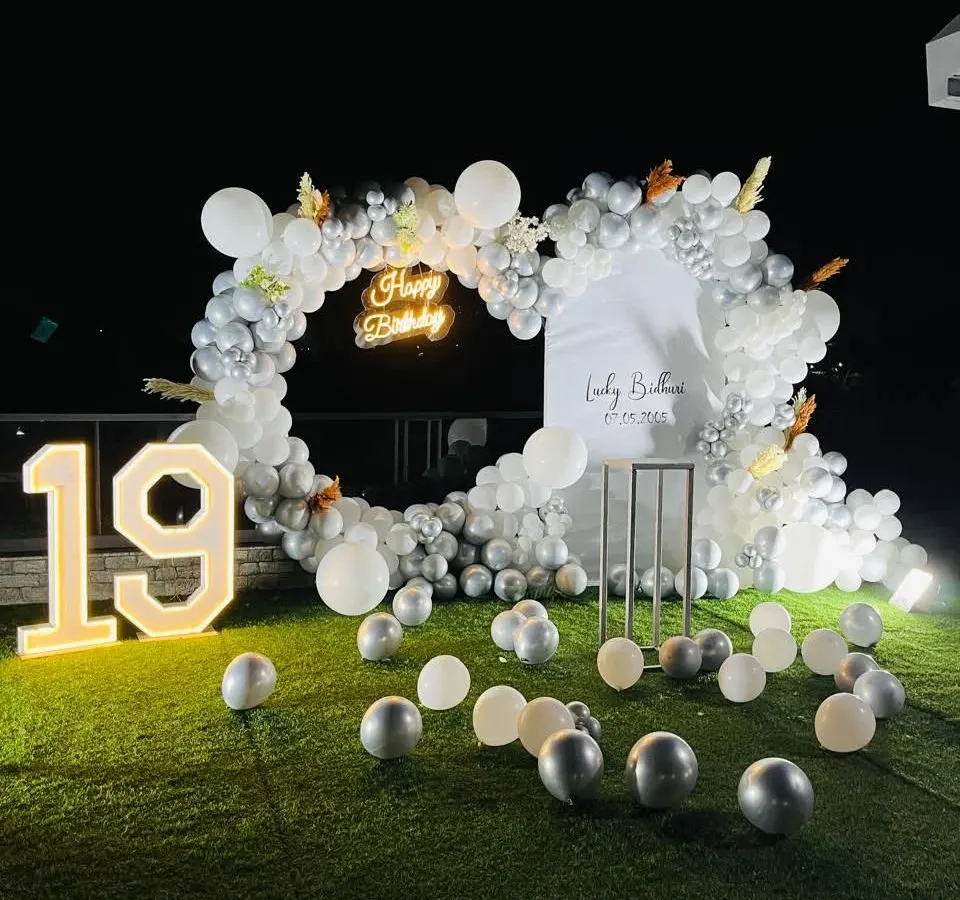An elegant and chic outdoor setup for a 19th birthday. The heart-shaped balloon frame in white and silver, paired with a "Happy Birthday" neon sign and a large marquee number, creates a perfect photo opportunity on the lawn.