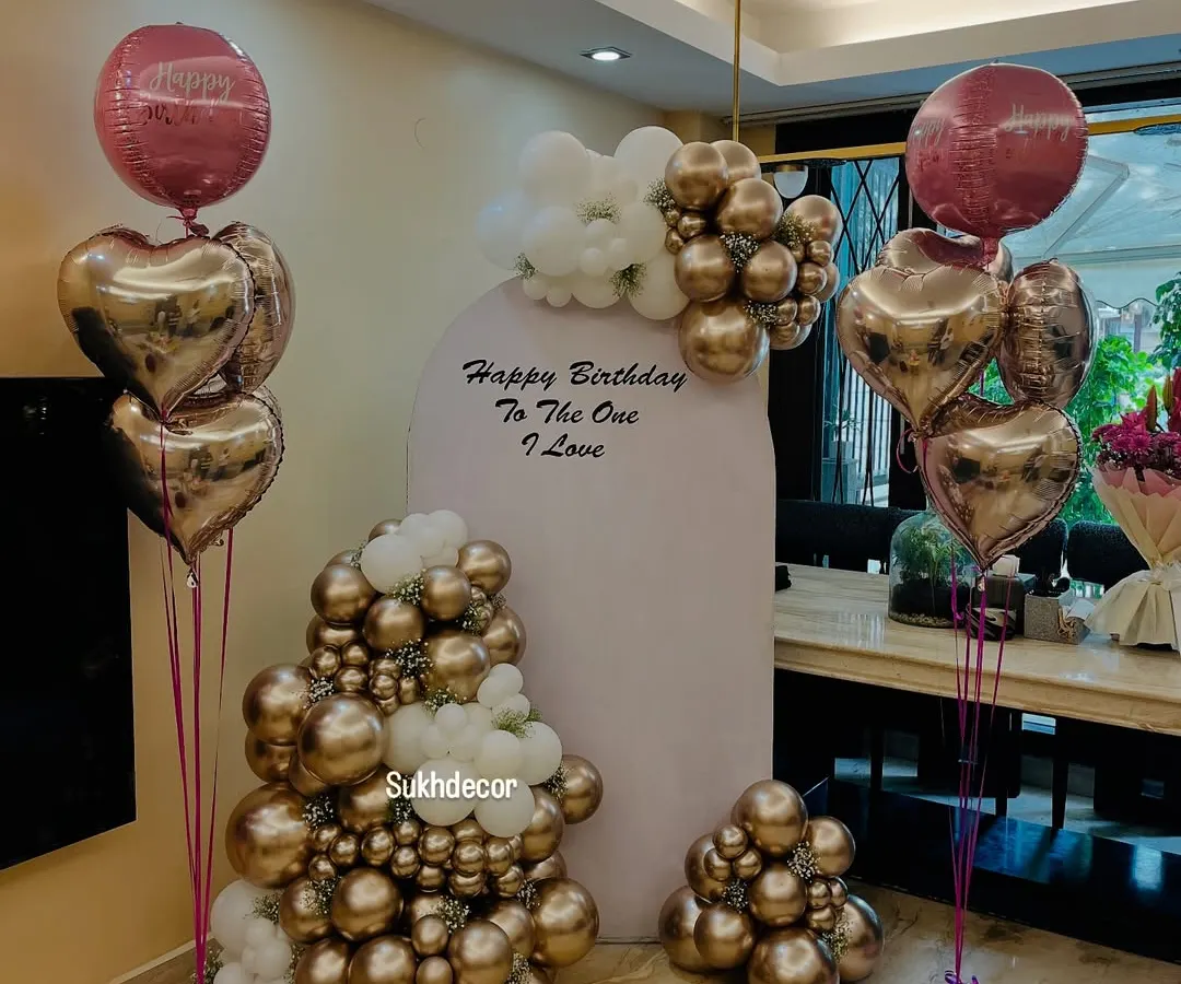 I create elegant and modern birthday celebrations, like this setup featuring a custom backdrop. The arrangement includes sophisticated chrome gold and white balloon clusters, along with heart-shaped foil balloons, perfect for a stylish and memorable party.
