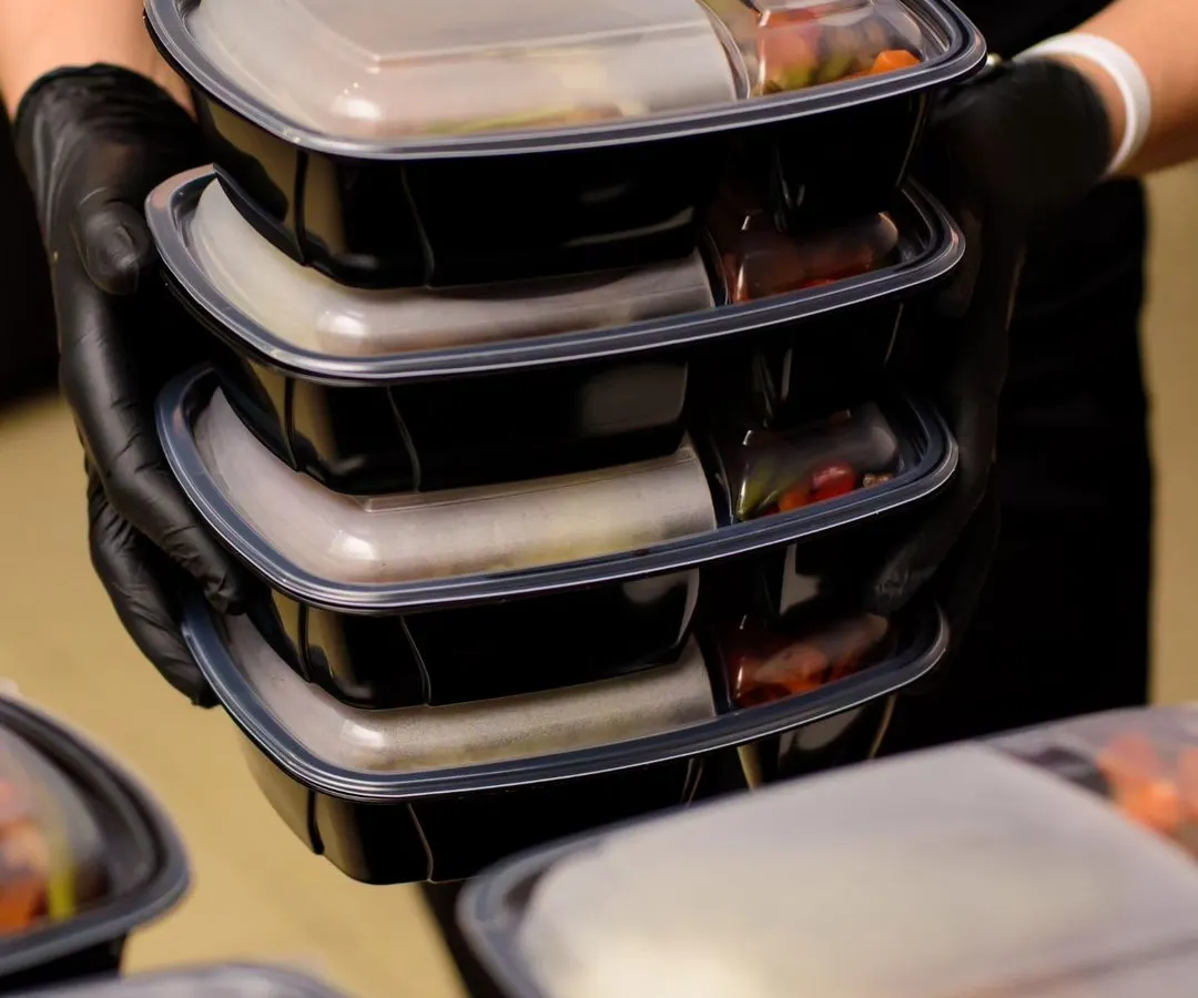 We ensure hygiene and convenience with our individually packed corporate meal boxes. Each meal is carefully prepared and sealed, making it a perfect solution for daily office lunches. This image shows our team handling a stack of meals ready for delivery.