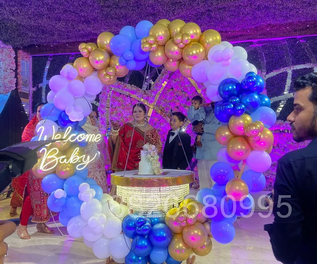 For a grand welcome baby celebration at a banquet hall, I created this large ring backdrop with blue, white, and gold balloons. The setup includes a 'Welcome Baby' neon sign and a central cake table, making it a stunning focal point for the event.