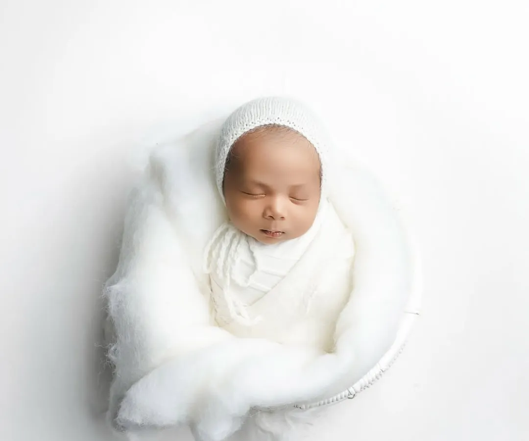 Wrapped in pure white, this 18-day-old newborn rests peacefully. My minimalist newborn photography focuses on their serene beauty and delicate features, creating a clean and timeless portrait.