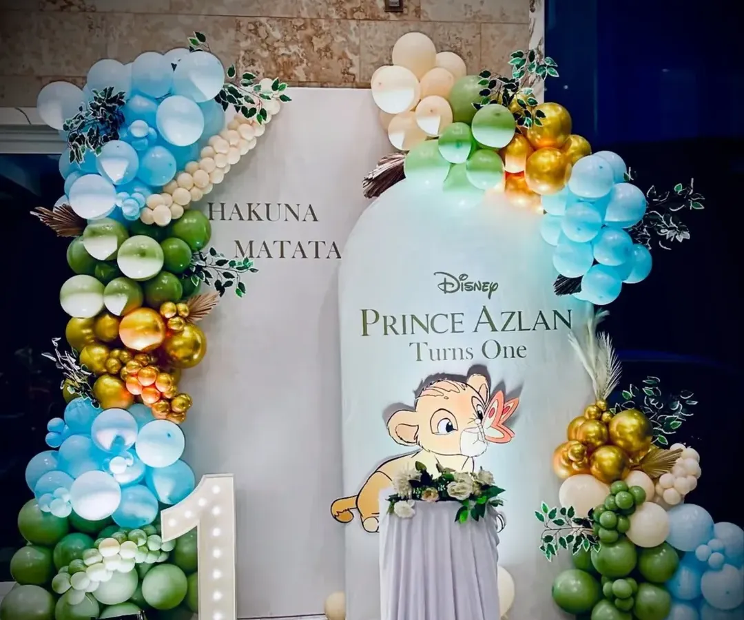 A "Hakuna Matata" themed first birthday party based on Disney's The Lion King. The setup includes a custom backdrop with baby Simba, balloon arches in jungle colors, and a light-up "1" marquee number to celebrate the big milestone.