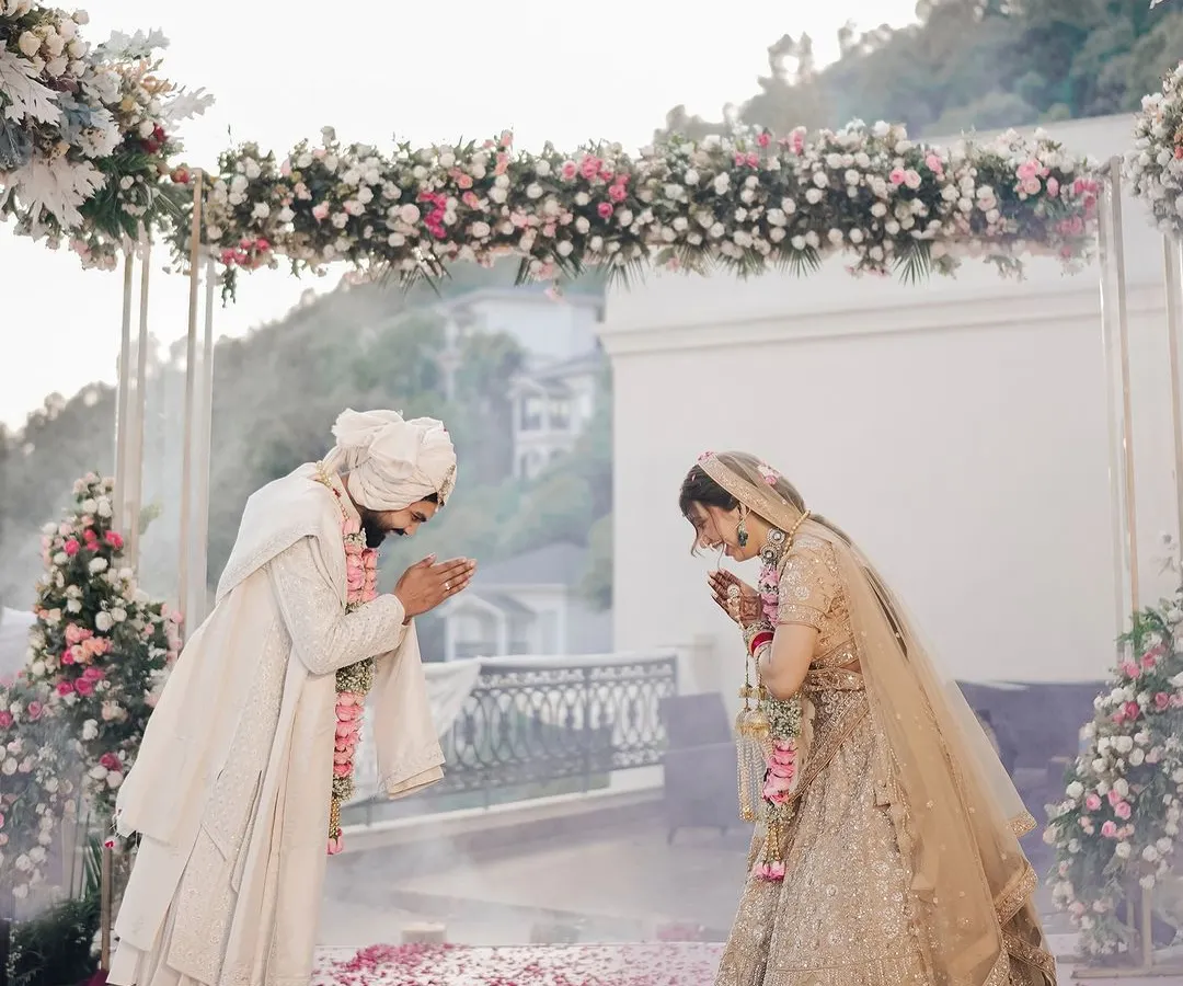 A moment of mutual respect and tradition at a scenic mountain wedding. The couple greets each other under a beautiful floral arch, with the vast hills providing a serene backdrop for their ceremony.