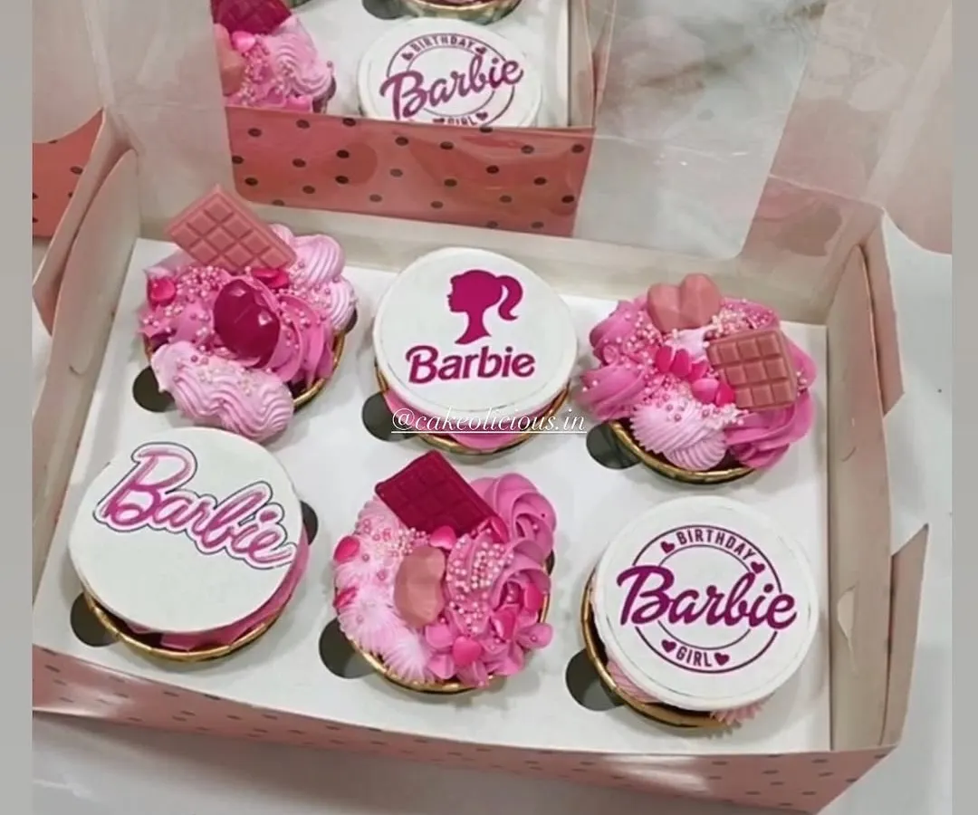 A box of custom Barbie-themed cupcakes, perfect for a birthday girl. Each cupcake is 100% eggless, with some featuring detailed edible prints and others topped with pink frosting, sprinkles, and chocolate pieces for a truly magical look.