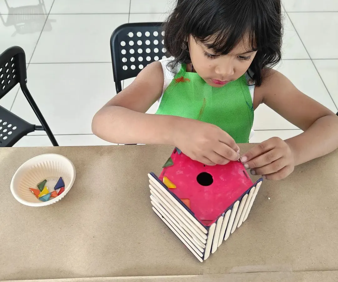 I love seeing the concentration on their faces! Here, a young artist is carefully assembling her own colorful birdhouse, a perfect take-home creation.