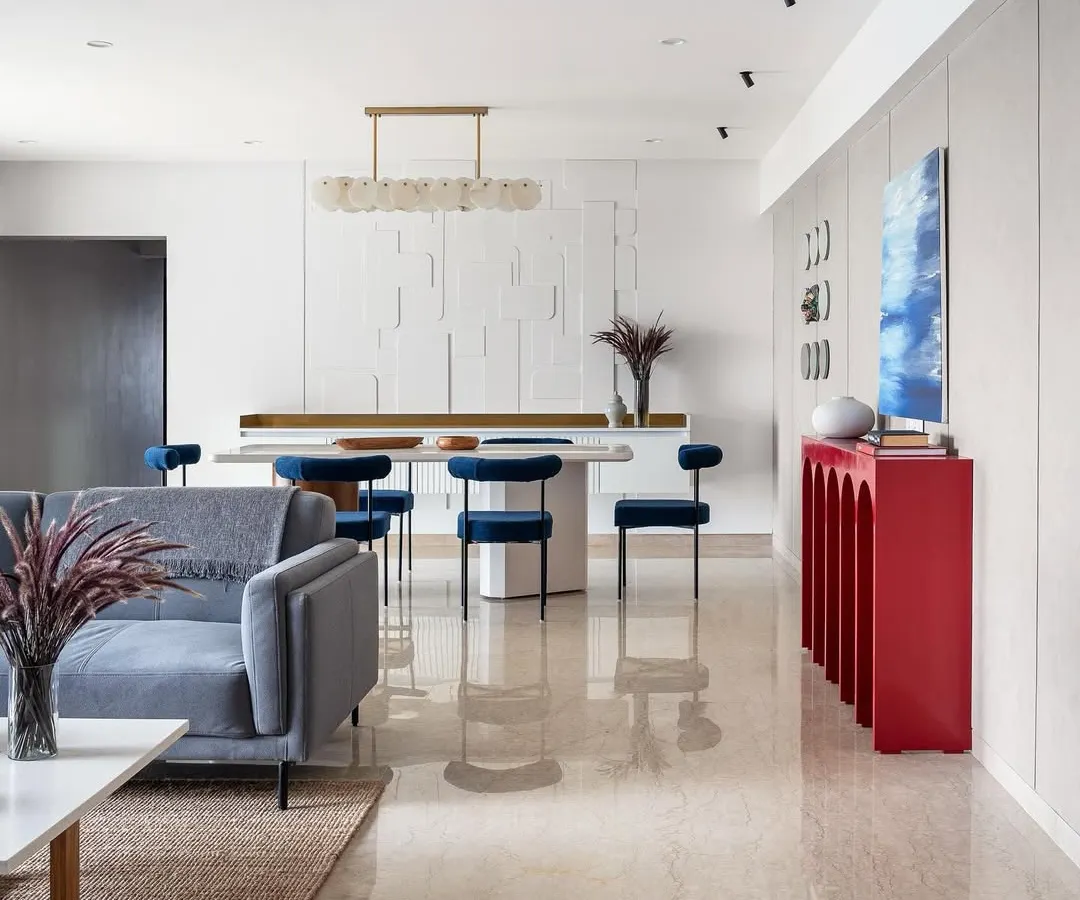 A glimpse into an open-plan living and dining area where modern design meets vibrant personality. The striking red console and rich blue velvet chairs add a bold splash of color, showcasing how we tailor each space to reflect our client's unique style while maintaining a cohesive, elegant flow.