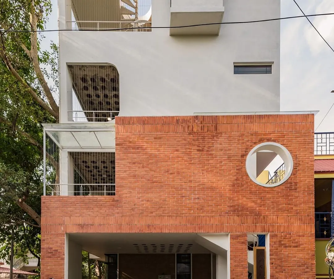 For this urban home in Bangalore, we contrasted a clean white facade with the raw texture of rat-trap bond brickwork. The circular window and spiral staircase are not just design elements; they are invitations to explore the different levels and how light moves through the space.