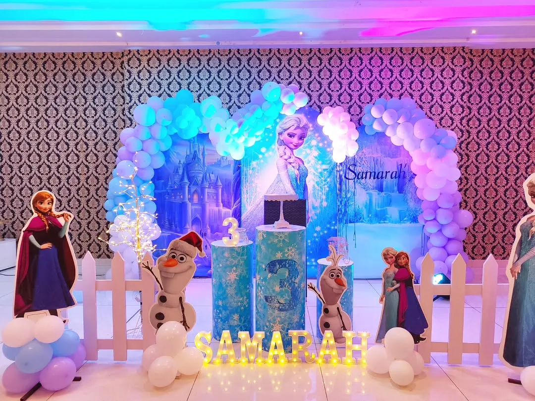 We bring the magic of Arendelle to life with this Disney's Frozen theme decoration. The backdrop features Elsa's ice castle, surrounded by a balloon arch in shades of icy blue and white, with life-size cutouts of Anna, Elsa, and Olaf.