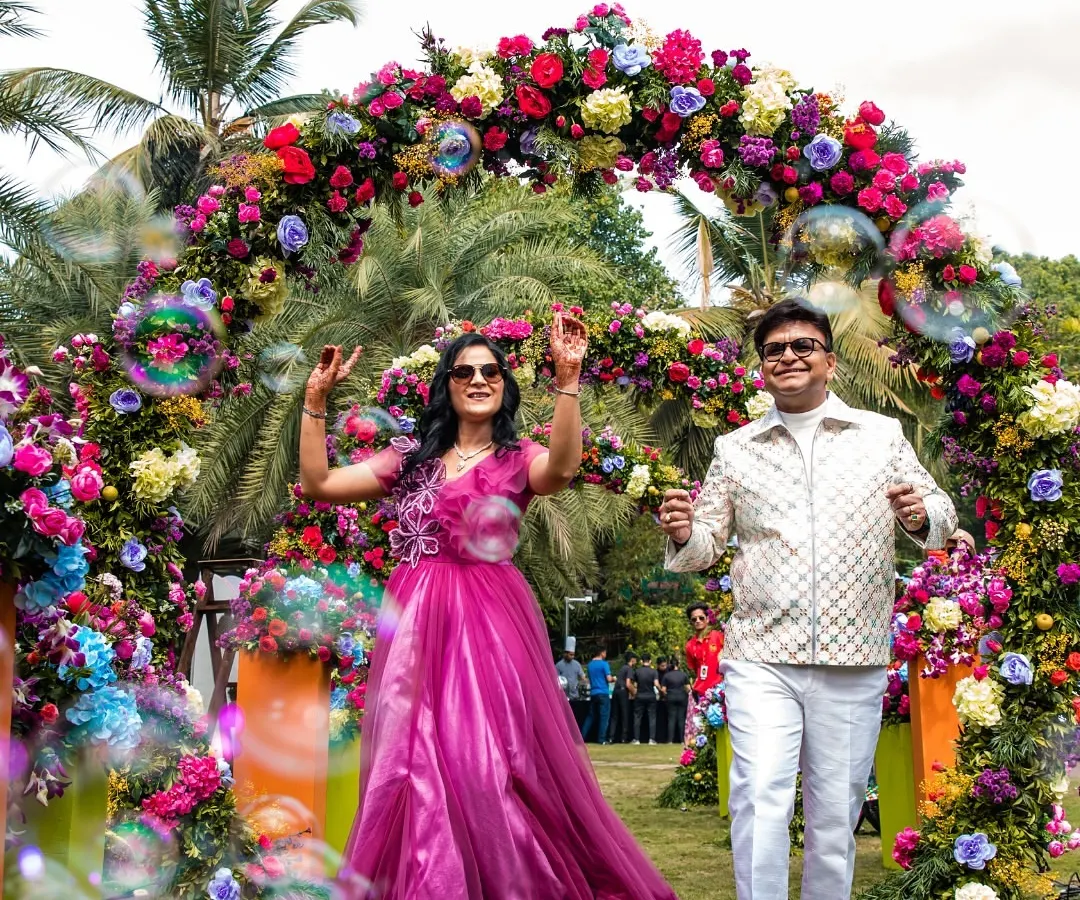 Nothing beats the pure joy of a milestone celebration. Here, the happy couple makes a grand entrance through a stunning tropical floral arch at their 25th-anniversary party in Goa, surrounded by bubbles and laughter.
