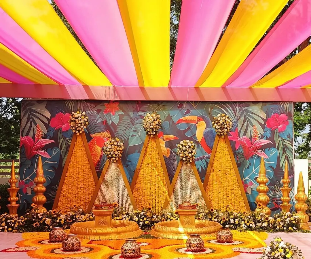 For this outdoor Haldi ceremony, I used a combination of bright pink and yellow fabric draping for the canopy. The backdrop features a custom tropical print, and the stage is decorated with marigold and tuberose floral structures.