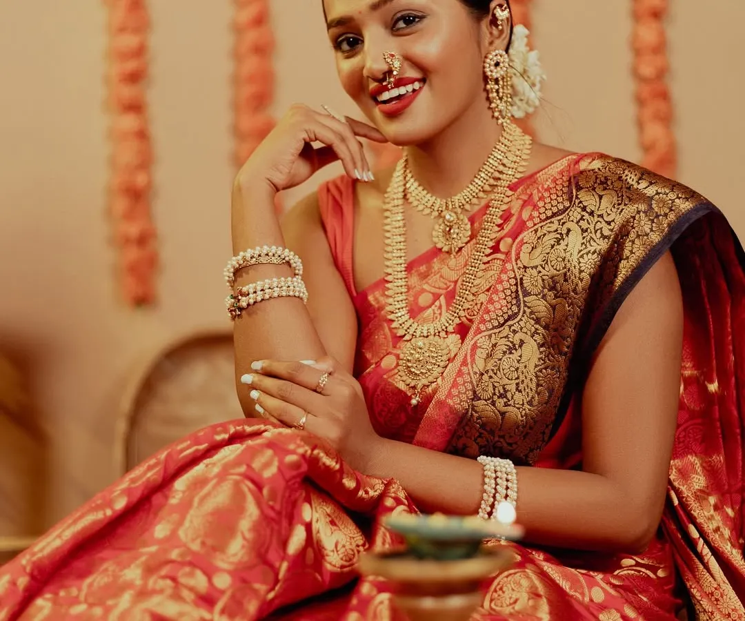 The pure joy of Diwali captured in a warm, ambient portrait. The model, dressed in a beautiful red and gold silk saree, shares a radiant smile, surrounded by the soft glow of diyas, perfectly embodying the festive spirit.