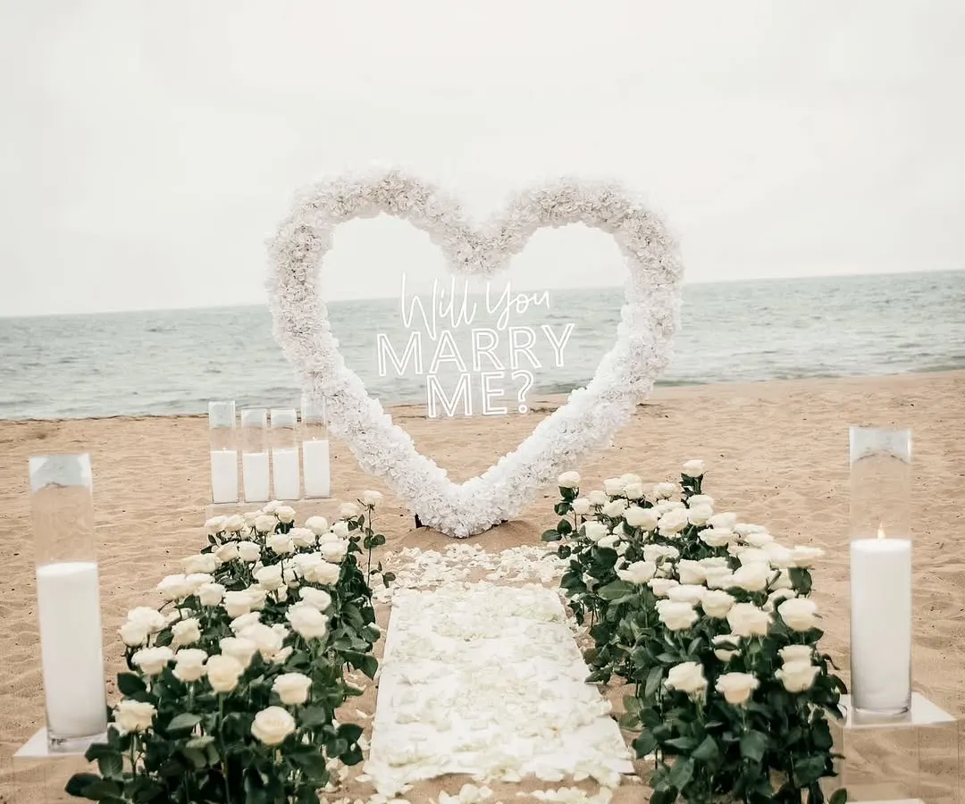 I transform beautiful locations like this beach into a private paradise for your proposal. This elegant setup features a white floral heart, a petal-strewn aisle, and candlelight to create a truly romantic engagement setting.