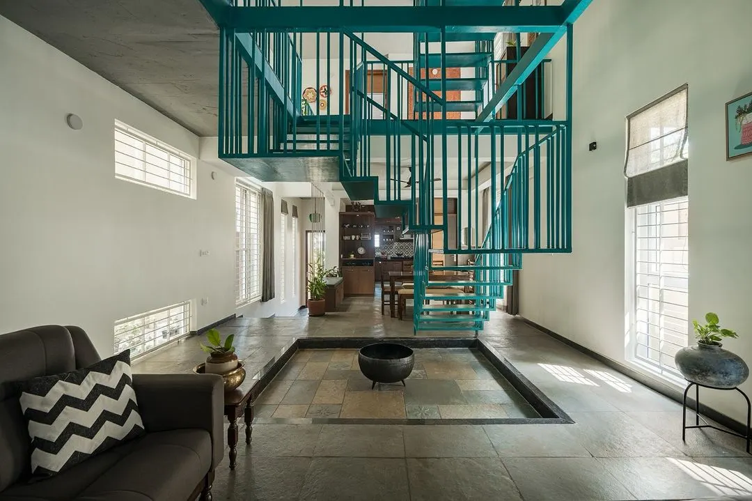 For the 'Jodi Mane' project, the staircase is more than just for circulation; it's the heart of the home. This suspended blue metallic stairway acts as a sculptural element, connecting spaces vertically while maintaining an open, airy feel around the central courtyard.