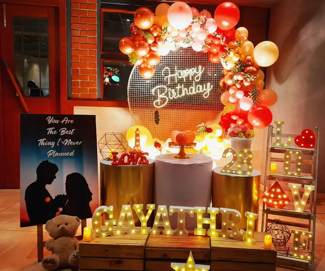 I designed this romantic birthday surprise for Gayathri. The setup features a warm, inviting color palette with a sequin backdrop, a custom silhouette poster, and lots of marquee lights spelling out her name and the word "LOVE" to create a truly personal and heartfelt atmosphere.