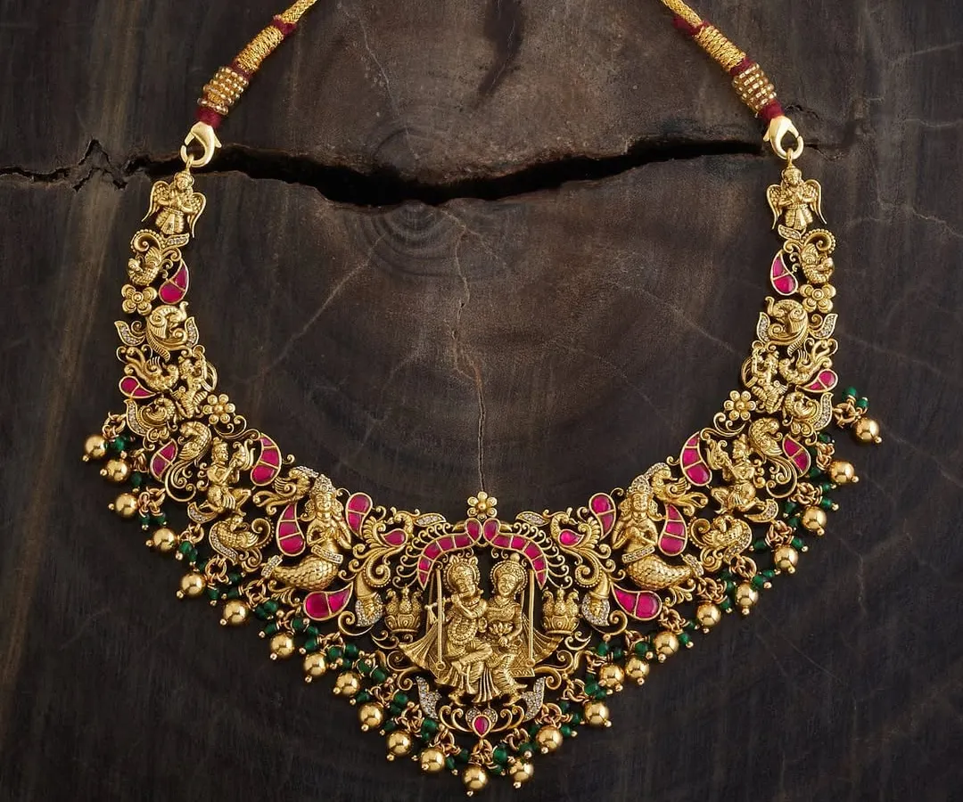This is a piece I am incredibly proud of, a true example of wearable art. It's a gold-toned temple necklace featuring an intricate depiction of Radha and Krishna, detailed with meenakari enamel in rich pink and green. This handmade choker is for those who appreciate divine motifs and exceptional craftsmanship in their traditional jewellery.
