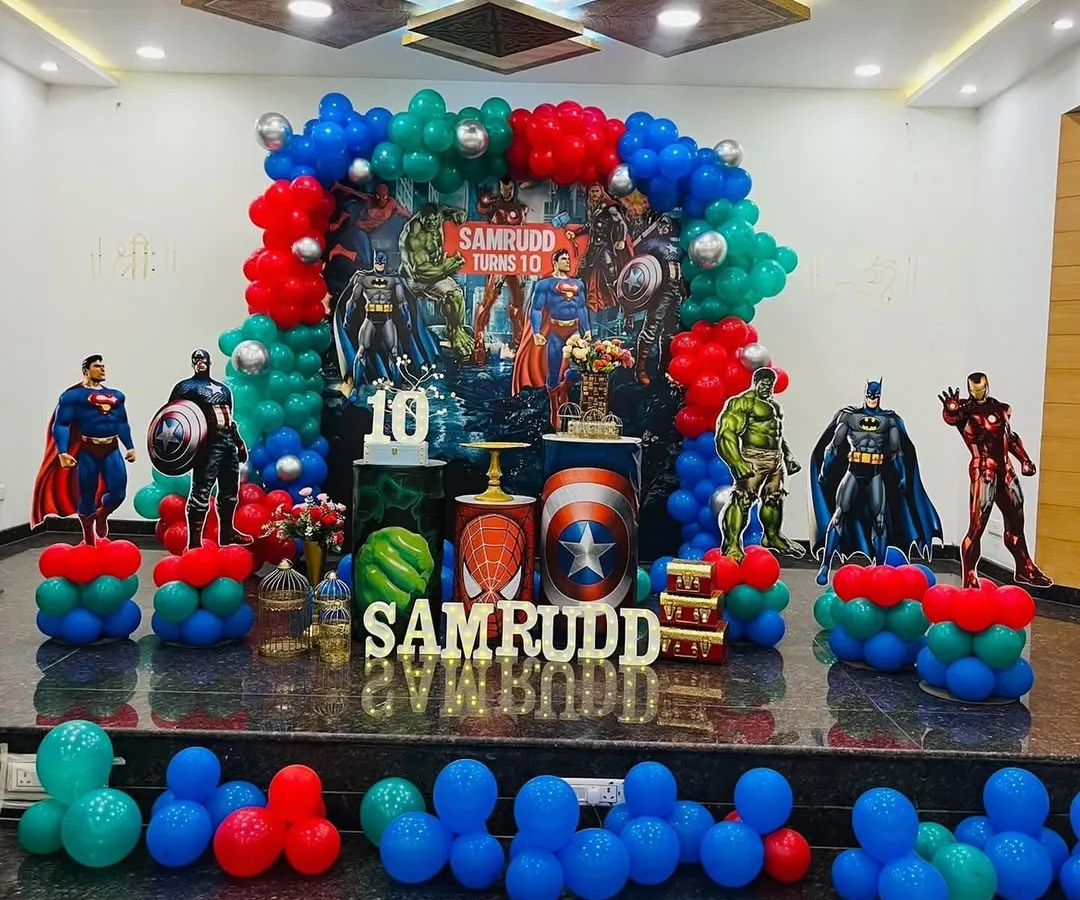 This is an action-packed Avengers theme party I designed for a 10th birthday. The stage features a custom backdrop with all the major superheroes, character cutouts of Batman, Superman, and Iron Man, and balloon columns in the classic red, blue, and green superhero colors.