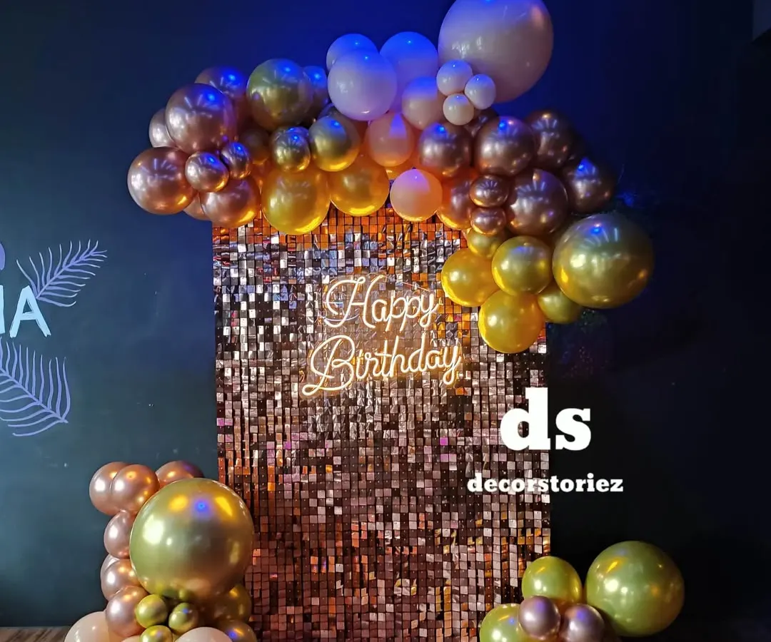 This close-up shows a glamorous photo corner we designed, featuring a shimmering rose gold sequin wall. The setup is framed by a cascade of metallic balloons and a 'Happy Birthday' neon sign, creating a perfect spot for party pictures.