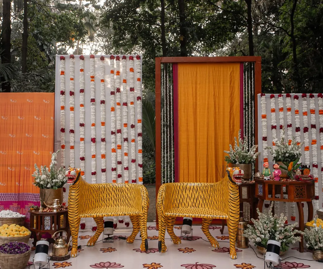 This reception stage was one of my absolute favorites to create, centered around the bride's cherished tiger chairs. We built the entire backdrop around them, using her mother's treasured sarees and complementing them with antique tables, traditional brassware, and vibrant Channapatna crafts for a truly personal and show-stopping result.