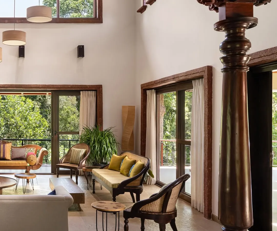 In the living room of the Dream Coffee Estate, a reclaimed antique wooden column stands as a silent witness to time, grounding the double-height space. We designed this room to be a conversation between old and new, where hand-chiseled stone floors and modern furnishings coexist under the expansive canopy of the Coorg forest visible through large glass doors.