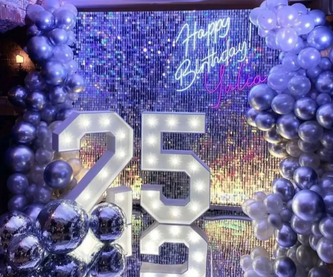 For a milestone 25th birthday, we created this ultra-glam photo corner. The setup features a silver shimmer wall that catches the light beautifully, a custom neon sign, and oversized marquee numbers, all framed by a cascade of metallic balloons.
