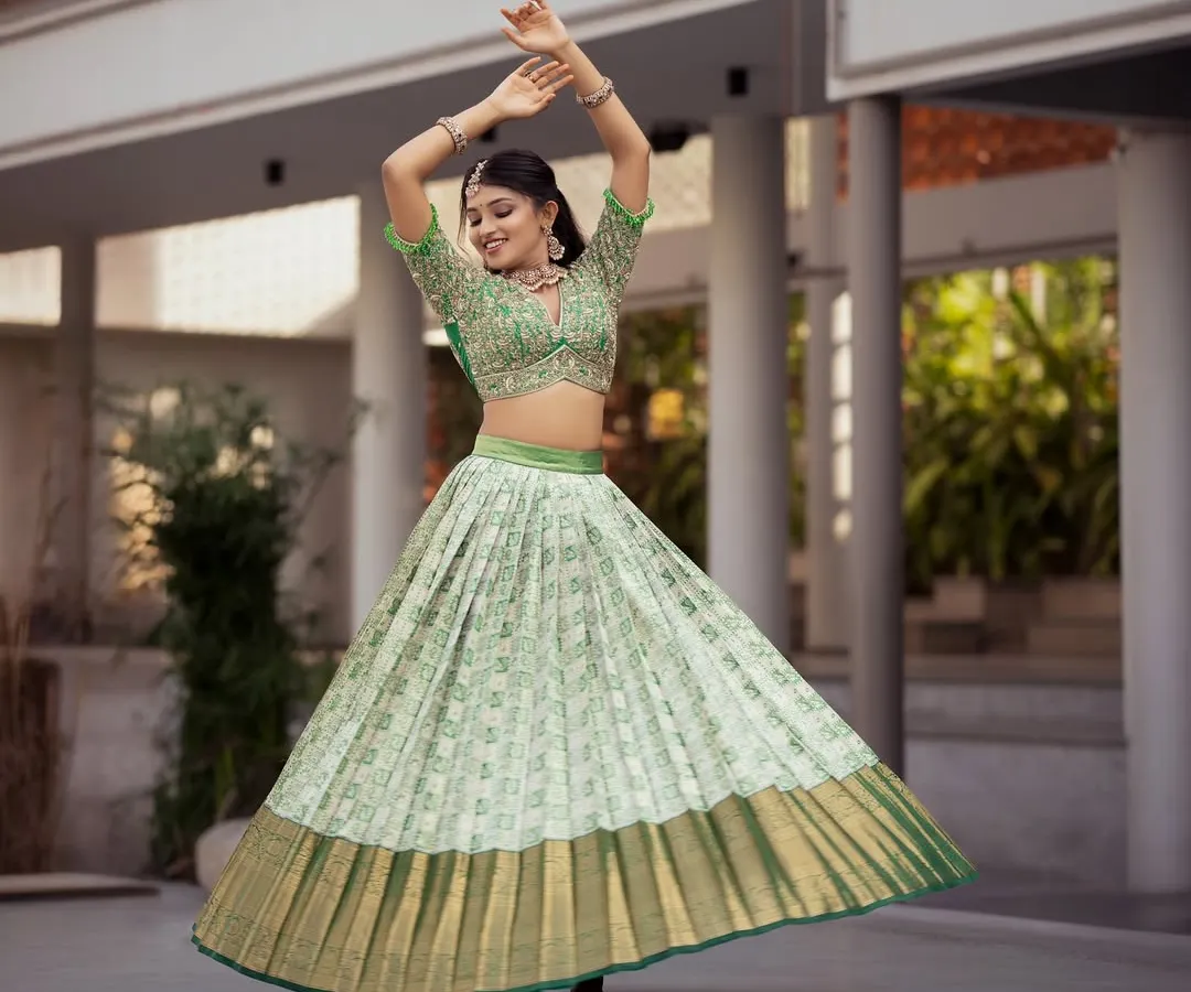 A vision of modern tradition, this Kanchi Pattu half saree in a vibrant pista green captures joyful movement. The pleated Kanchipuram silk skirt creates a beautiful flare, paired with a heavily embroidered blouse, making it a perfect choice for an engagement, sangeet, or half saree ceremony.