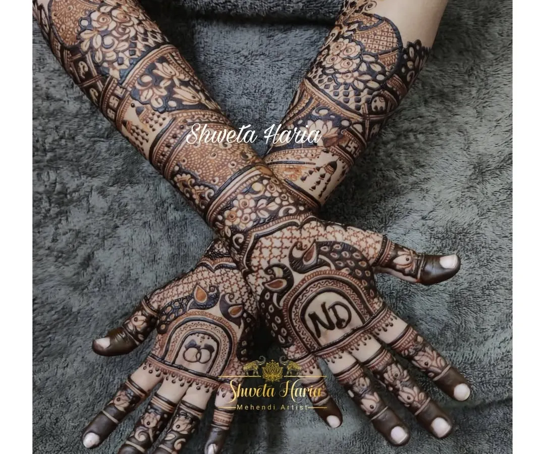 For your engagement, we can create a design that is both traditional and personal. This intricate mehendi features the couple's initials, 'ND', and interlocking rings, surrounded by classic peacock and floral motifs that extend up the forearm.