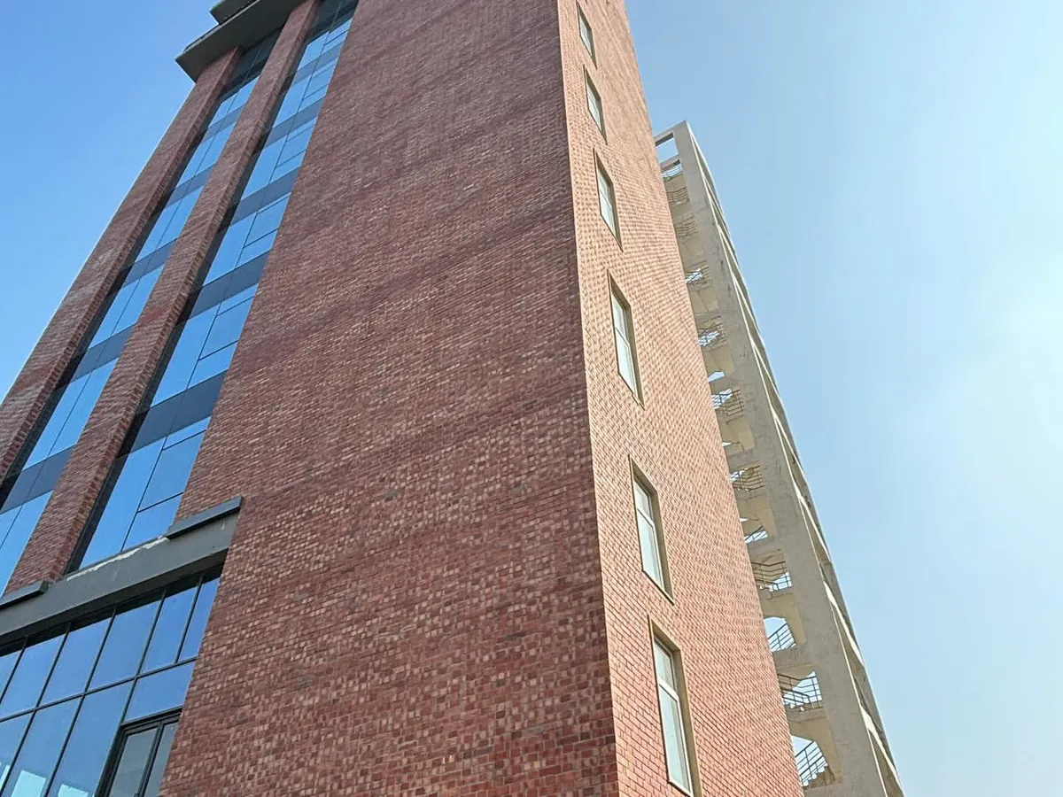 An upward view of a recently completed office building, capturing the powerful interplay between the solid, earthy texture of exposed brick and the sleek, reflective quality of a modern glass curtain wall.