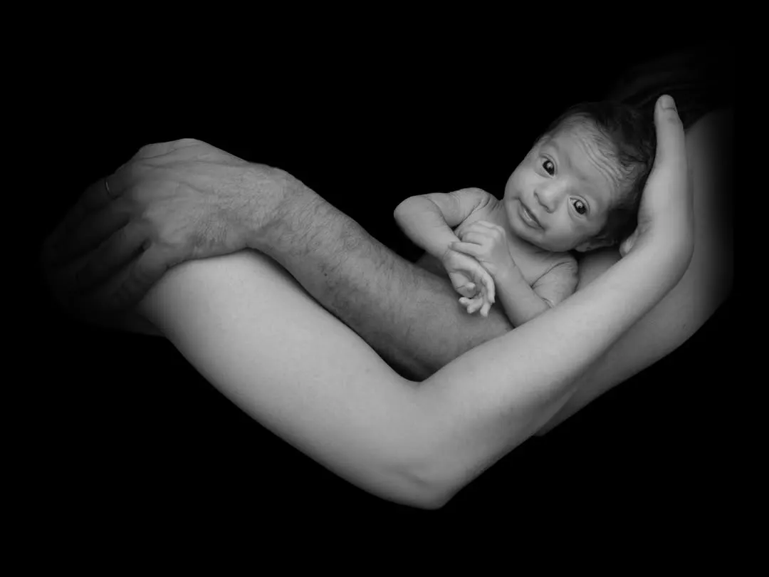 This black and white portrait captures a newborn held securely in the loving arms of their parents. I focus on creating these powerful, emotional images that highlight the family's bond.