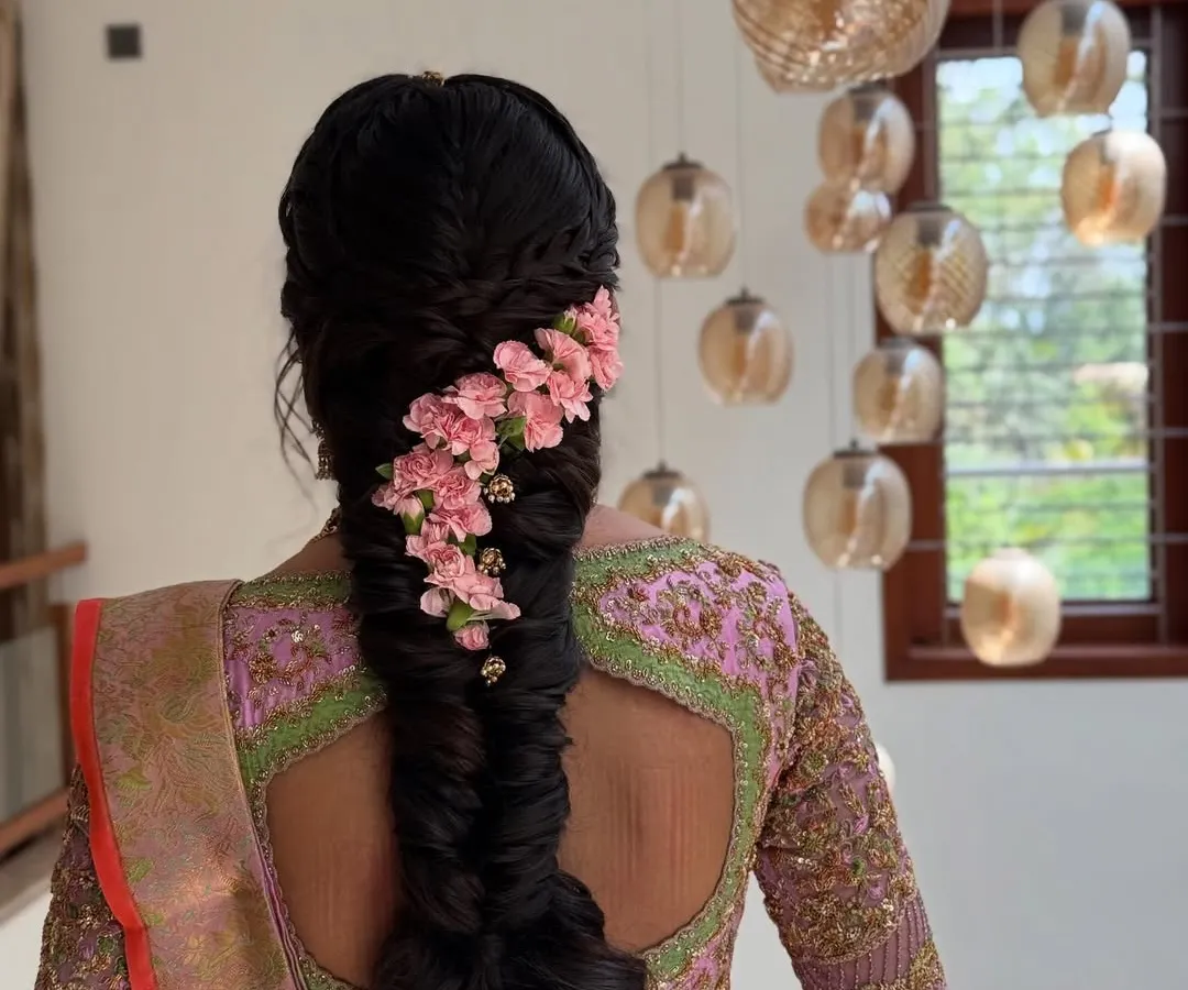 For a softer, more romantic bridal style, I designed this intricate fishtail braid adorned with a cascade of delicate pink flowers. This look is perfect for pre-wedding events like an engagement or sangeet, blending traditional braiding techniques with a modern floral touch.