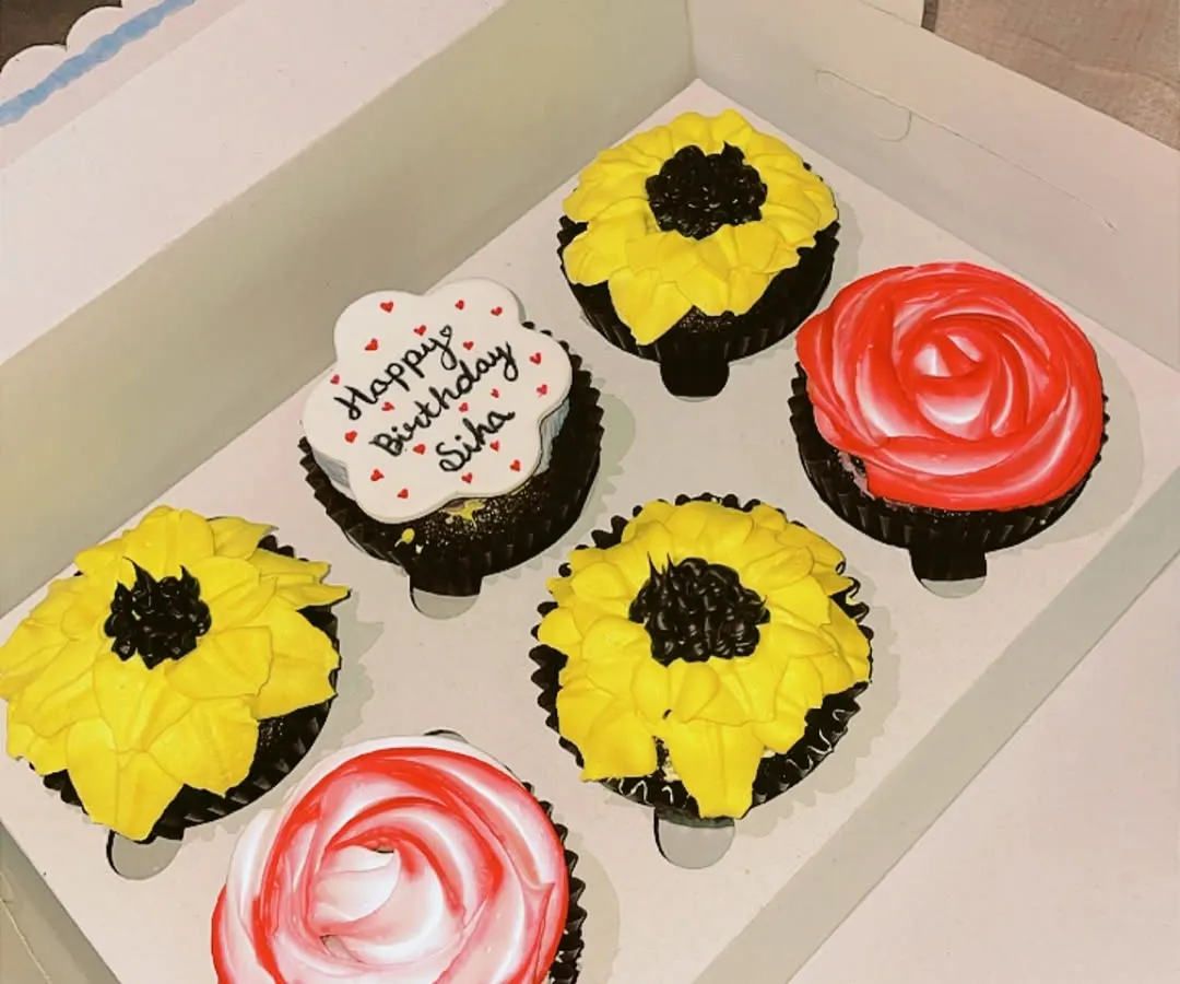 A custom box of six eggless cupcakes designed for a birthday. This set features hand-piped sunflower and rose designs, along with a personalized cupcake with a 'Happy Birthday' message. I can create themed cupcake boxes for any occasion.