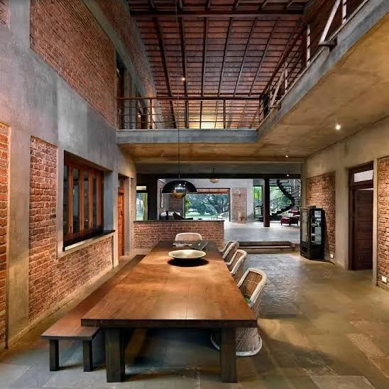The dining area at The Mango House in Alibag is the heart of the home. Here, exposed brick walls, a double-height ceiling with terracotta tiles, and a large wooden table create a space that is both grand and grounded, perfect for conversations that last for hours.