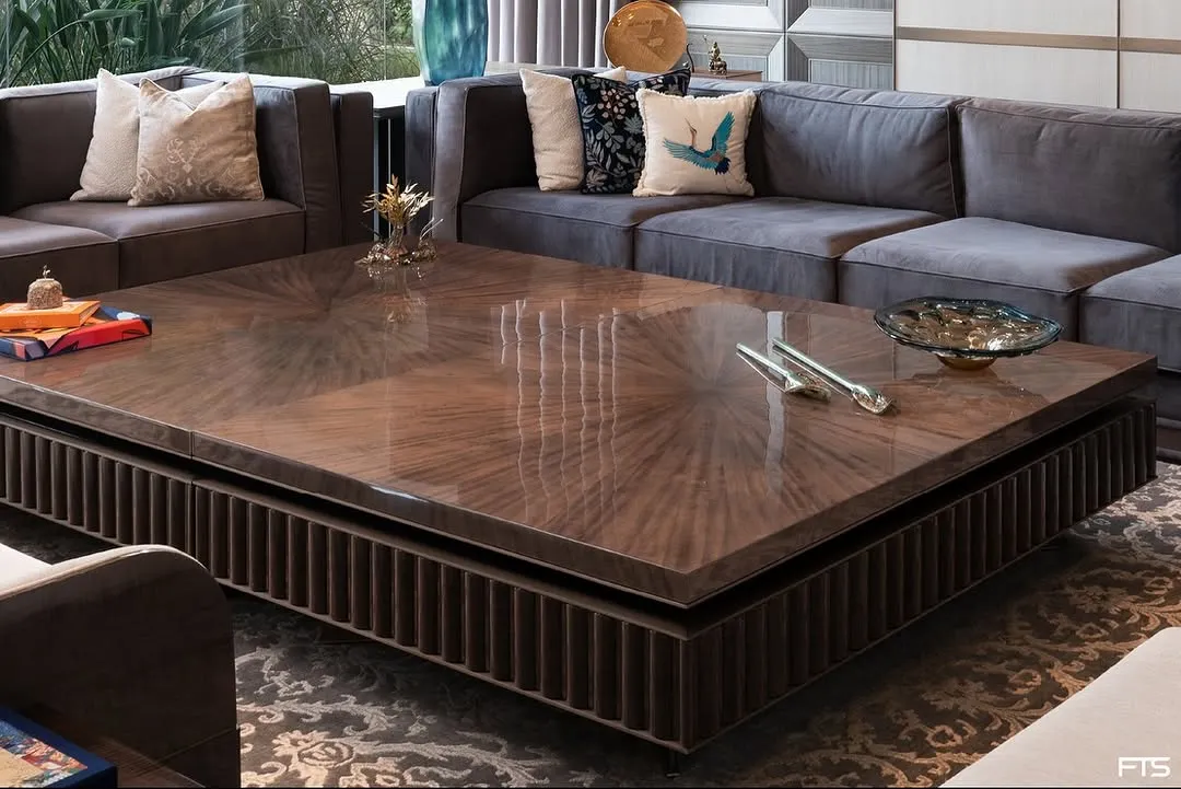 The centerpiece of this New Delhi farmhouse living room is a custom-designed coffee table with a starburst-patterned top in dyed figured veneer. Its substantial form is balanced by intricate wooden fluting and bronze detailing, creating a focal point that is both a statement and an invitation to gather.
