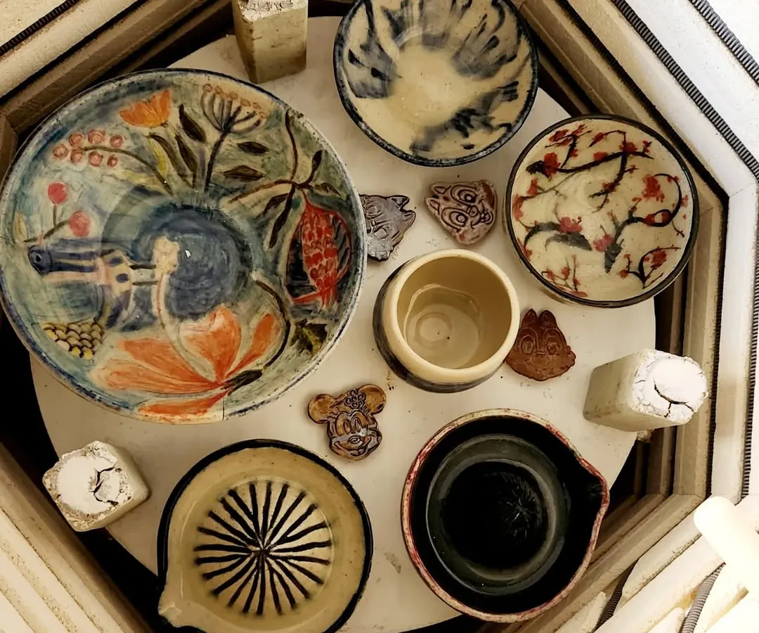 A glimpse of various pieces fresh from the kiln. You can see a hand-painted plate, a citrus juicer, and several bowls, each with its own unique glaze and character, ready to find a new home.