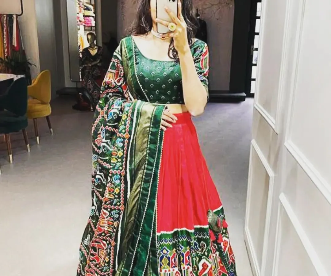A beautiful art silk lehenga set in a classic red and green combination. The highlight is the intricate Patola and Bandhani print dupatta, which adds a traditional touch. This complete set is perfect for weddings or festive parties.