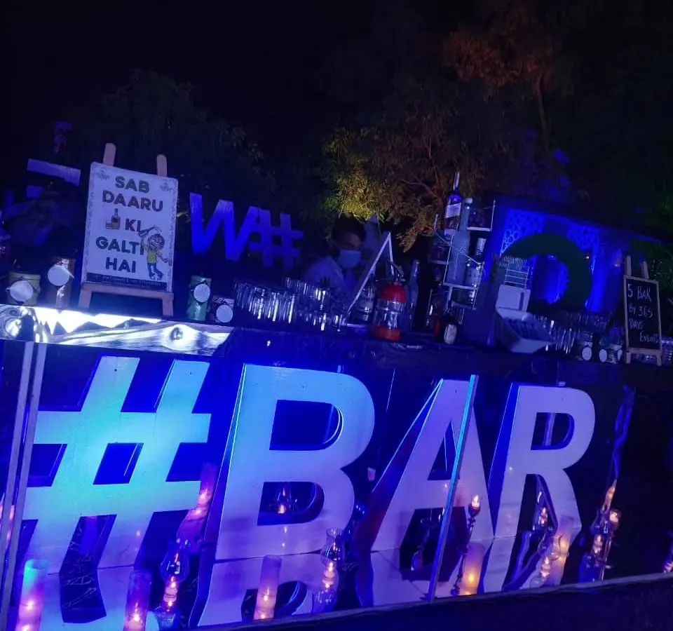 I love adding a modern and fun touch to evening events. This bar setup features a large, backlit LED sign and cool blue lighting, creating a vibrant atmosphere perfect for a sangeet or cocktail night.