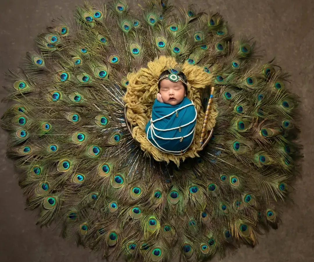 Creating a touch of magic with my popular Krishna-themed newborn session. This wide-angle shot shows the beautiful setup with a full display of peacock feathers, turning your baby's first portraits into a divine work of art.