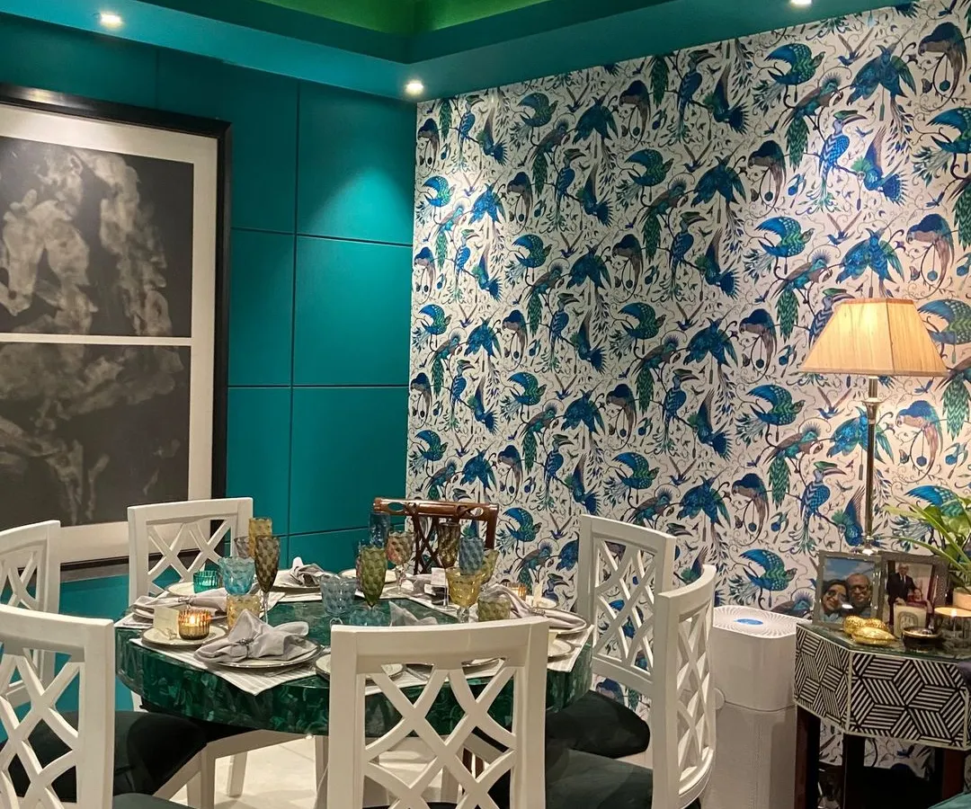 We love to embrace bold design choices that reflect our client's personality. This eclectic dining room features a dramatic teal wall and a vibrant, bird-patterned wallpaper, creating a rich and immersive experience. The custom malachite stone tabletop and hand-carved white chairs serve as statement pieces, making every meal an occasion.