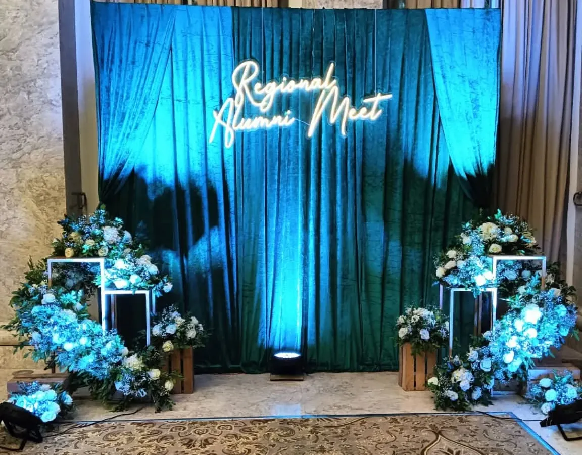 For this regional alumni meet, I designed a sophisticated stage with a rich green velvet curtain and a custom neon sign. The blue uplighting and floral arrangements create a premium and memorable atmosphere for formal gatherings.