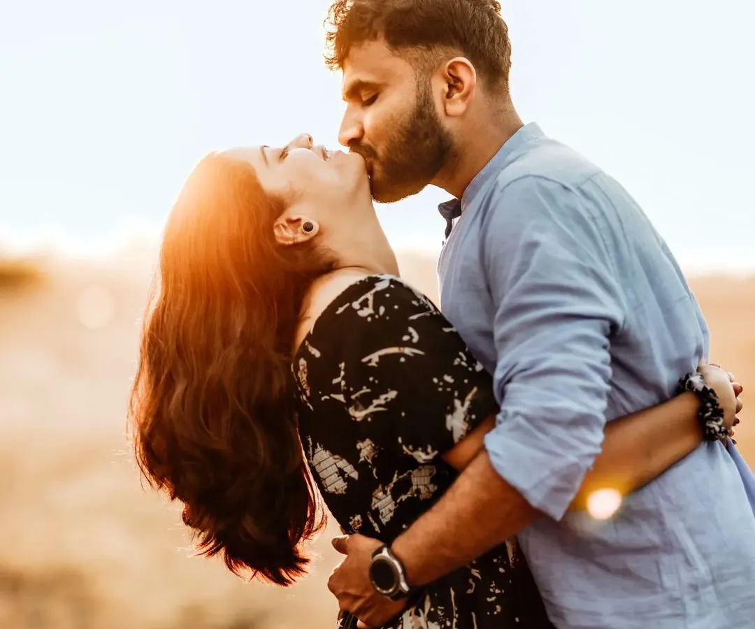 The golden hour is a magical time for photography. Here, the warm, setting sun creates a beautiful flare, highlighting the couple's intimate kiss and turning a simple moment in a field into something truly cinematic and unforgettable.