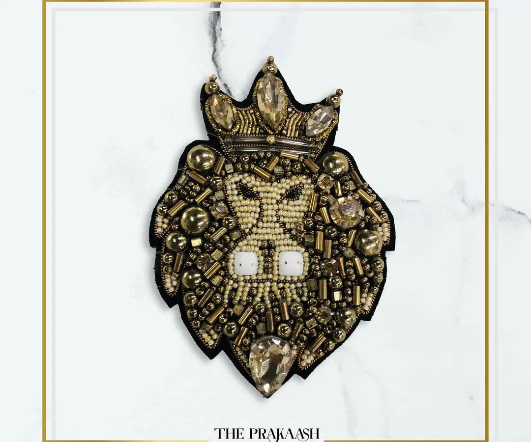 This hand-embroidered patch showcases a majestic lion's head with a crown, crafted with beads, stones, and metallic thread. It's a statement appliqué designed to add a regal touch to blazers, jackets, or bags.