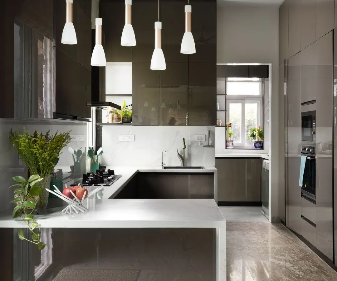 This modern kitchen is the heart of the home, featuring sleek, high-gloss grey cabinetry and a pristine white quartz countertop. The design focuses on clean lines and an efficient U-shaped layout, with integrated appliances and pendant lighting that adds a touch of warmth and style.
