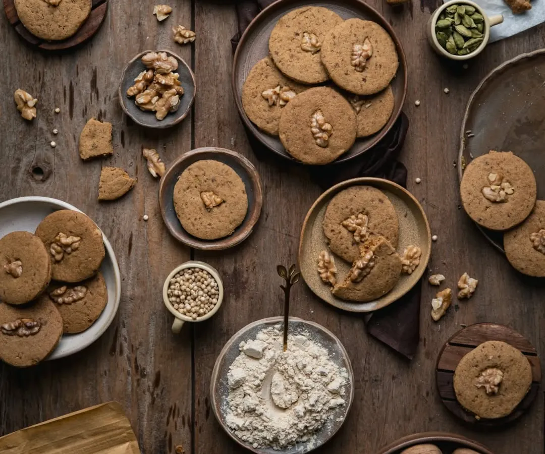 A flatlay of wholesome jowar walnut cookies, showcasing the raw ingredients and the delicious final product. I love creating these detailed, textured scenes that tell the story of a food product from scratch, making it feel both artisanal and inviting. This is a great example of food styling for healthy snack brands.