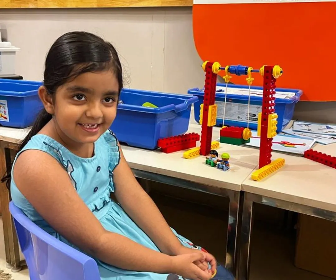 A student in our Tinkering summer camp proudly displays her working swing set, built using a LEGO education kit. Our program for ages 5 and up introduces core engineering and mechanics concepts through hands-on, playful creation.