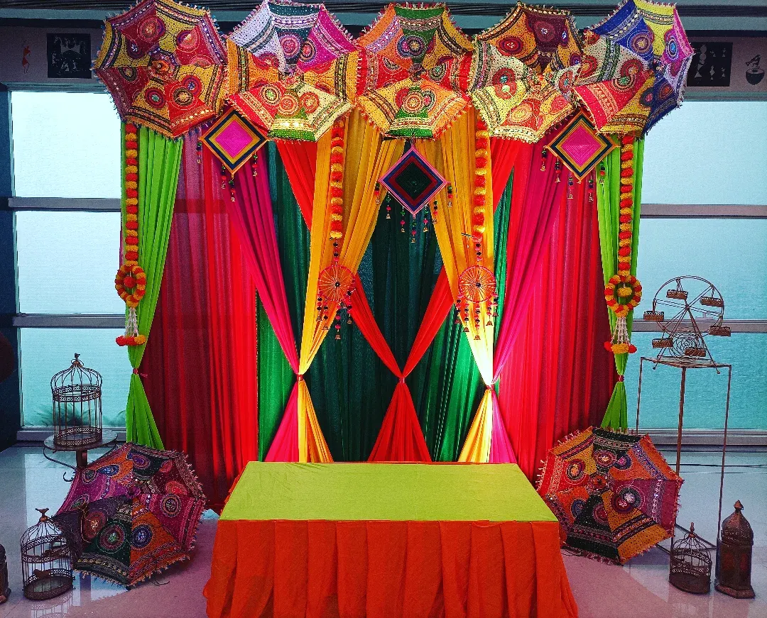 For a traditional godh bharai, I love using vibrant colors. This setup features a backdrop of bright drapes in green, pink, and yellow, topped with beautiful Rajasthani embroidered umbrellas for a truly festive look.