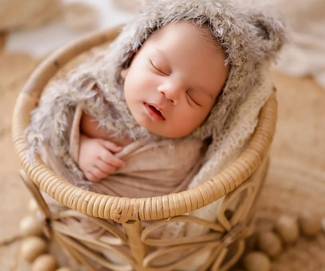 I love capturing newborns in their sleepy, peaceful state. This little one is nestled in a soft basket, wearing an adorable fuzzy bear hat from my studio's collection.