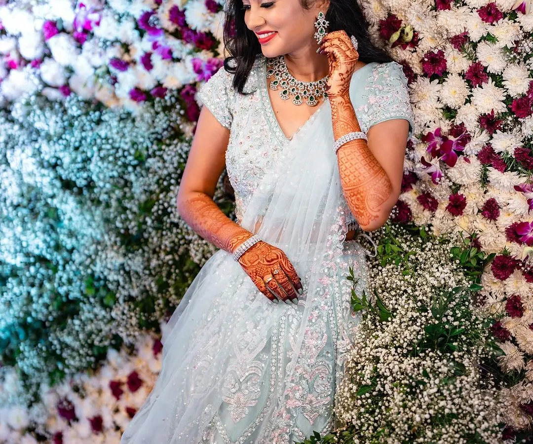 For a modern reception or sangeet, we can create something truly magical. I loved styling this shimmering lehenga with soft, romantic curls and a makeup look that felt glamorous yet effortless against this beautiful flower wall.