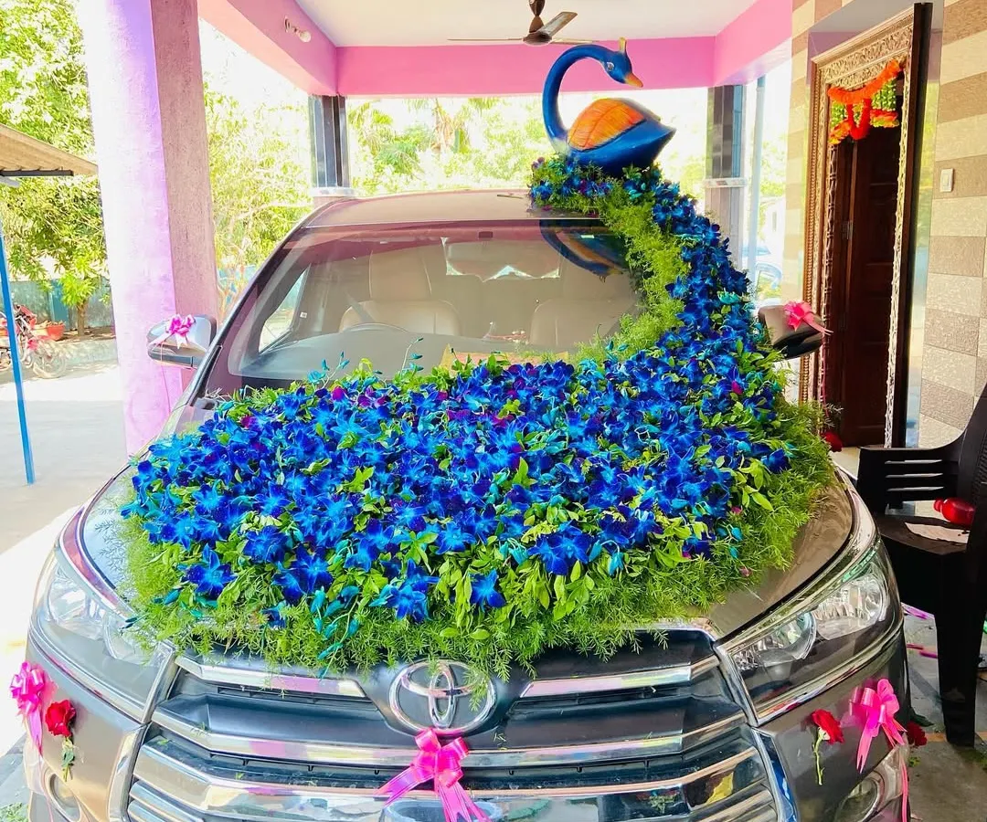 This is my signature peacock themed wedding car decoration on a Toyota Innova. The design features a beautiful peacock figure with a long, flowing tail of blue orchids and greenery covering the bonnet, making it a true showstopper.