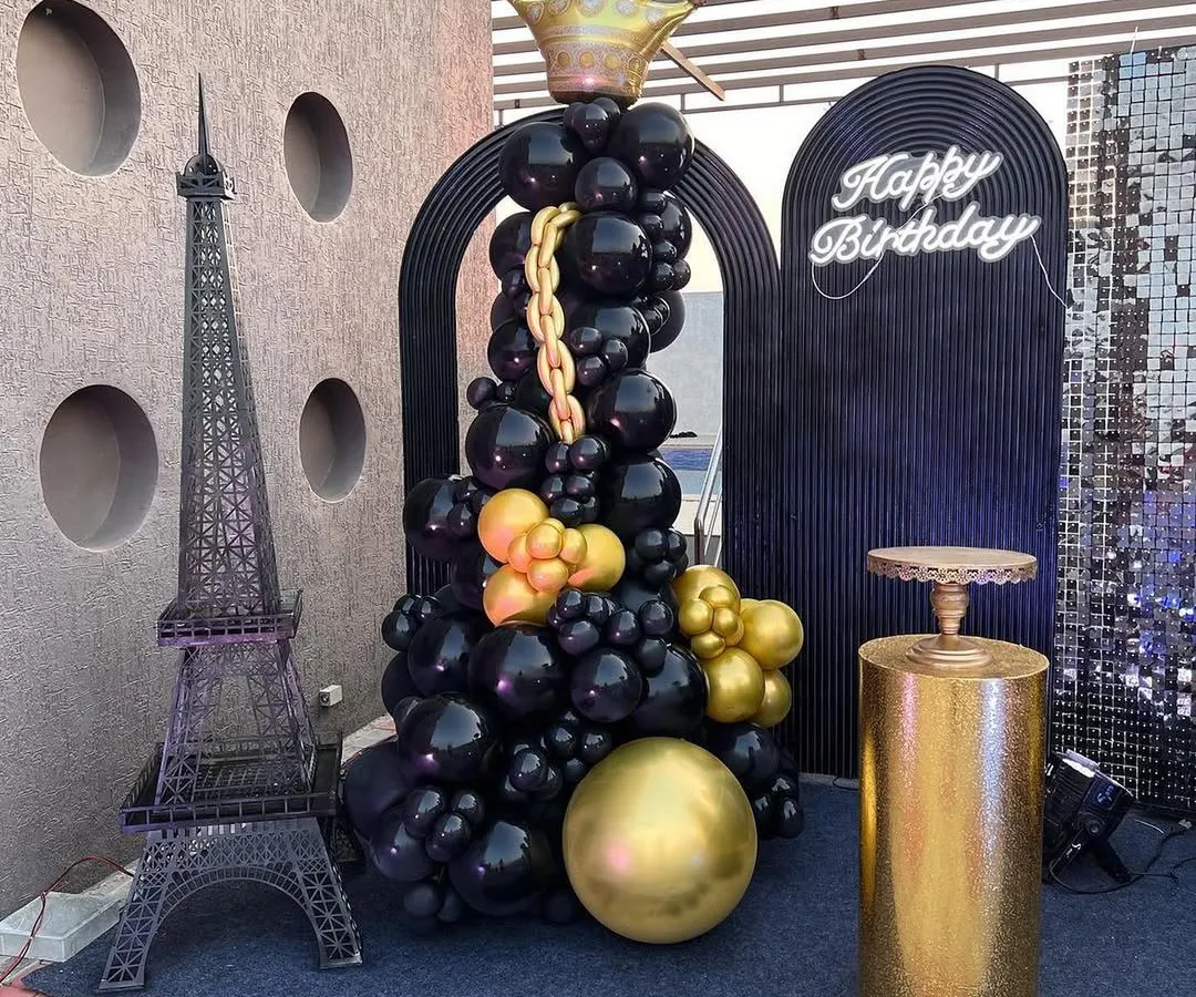 For a sophisticated adult birthday on a terrace, I designed this chic black and gold theme. The setup includes a statement balloon sculpture with a crown, a miniature Eiffel Tower for a touch of Parisian elegance, and a glowing neon sign, creating a perfect photo-op spot.