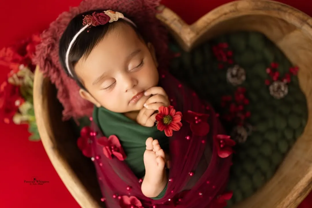 This portrait captures the peaceful sleep of a newborn, swaddled in festive red and green. The heart-shaped wooden bowl is one of the many props I have in my Navi Mumbai studio to create unique setups.