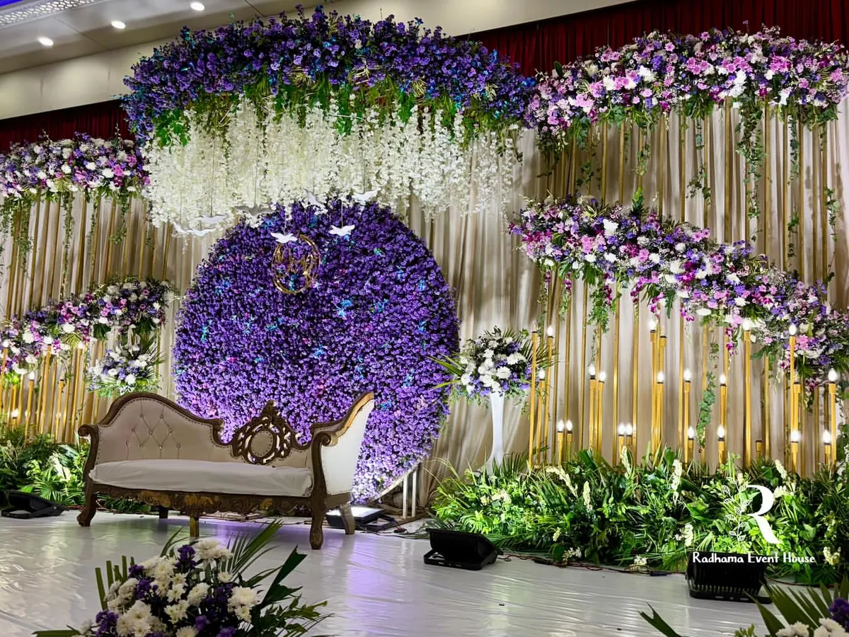 For this monsoon wedding reception, we designed a romantic stage drenched in shades of purple. A massive circular backdrop of purple chrysanthemums, paired with hanging white wisteria and lush greenery, creates a dreamy, immersive floral experience.